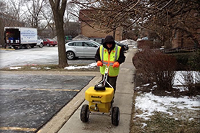 man pushing a salt dispenser on an icy sidewalk